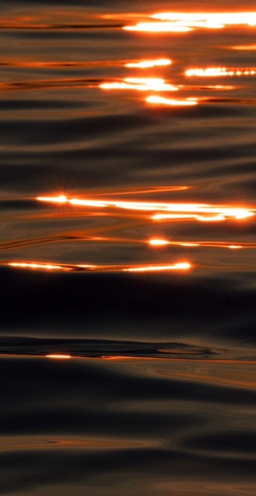 Warm orange glare and reflections on wavy water surface creating serene abstract wallpaper background