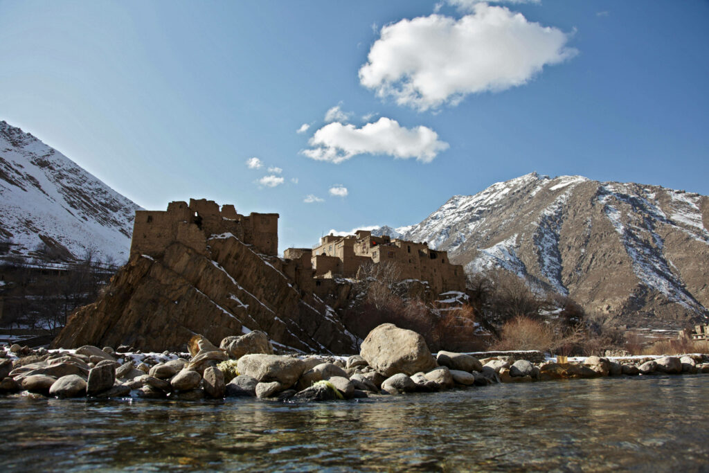Ancient stone structures by Panjshir River with snow-capped mountains and clear flowing water Wallpaper