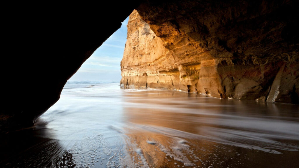 Sunlit sea cave at Pomponio State Beach with smooth water and golden cliffs coastal wallpaper