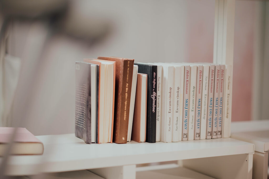 Minimalist white shelf with pastel and white covered books creating serene library wallpaper