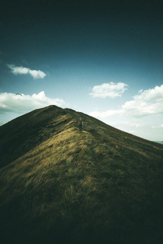Lone figure on grassy ridge under vast sky in Peak District National Park serene mountain view Wallpaper