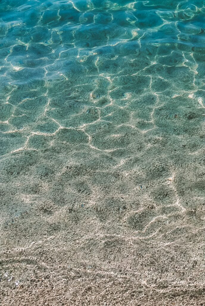 Smooth pebbles under clear water with sunlight reflections and gentle blue green ripples wallpaper background