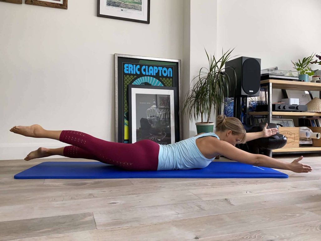 Woman doing Pilates swimming exercise on blue mat in sunlit room with music posters background Wallpaper