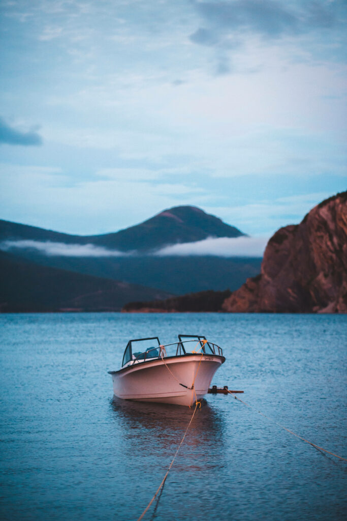 Pink boat on calm blue water with mountains and clouds peaceful nature wallpaper background
