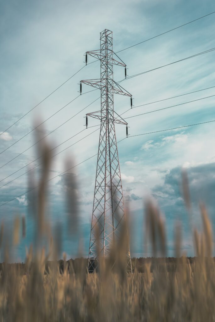 Tall metal power line tower over golden grass fields under partly cloudy blue sky landscape wallpaper