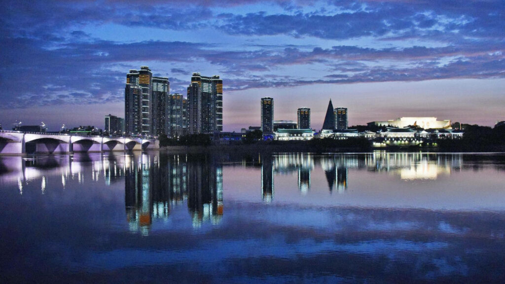Stunning Pyongyang Cityscape Wallpaper: Serene River Reflection Dusk