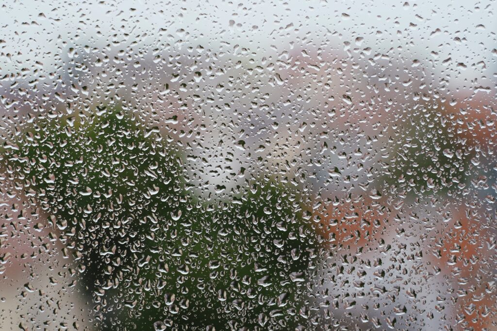 Serene Rain Droplets Wallpaper: Glass Surface with Blurred Greenery