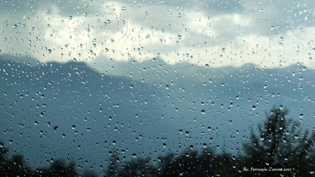 Serene Rain-Drenched Window Wallpaper: Blurred Mountain and Tree View