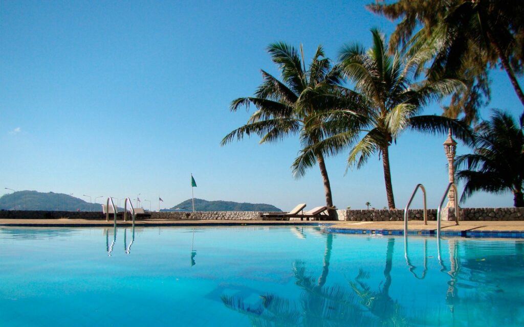 Serene resort pool with palm trees and distant hills under clear blue sky for relaxation Wallpaper