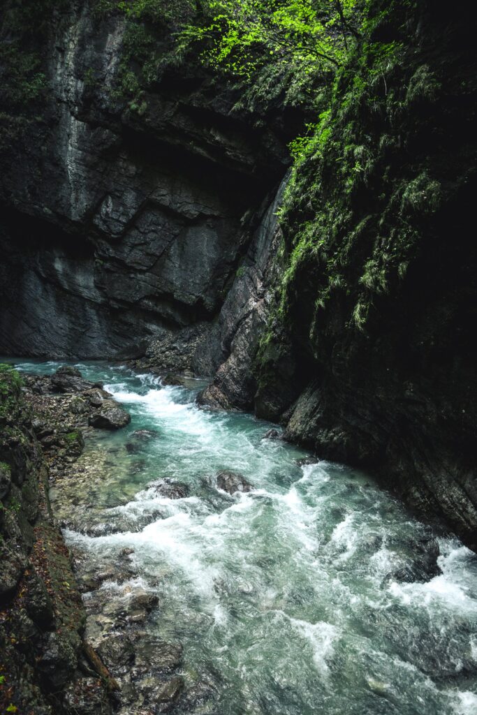 Serene river flowing over rocks with lush green trees and dark rugged cliffs wallpaper background