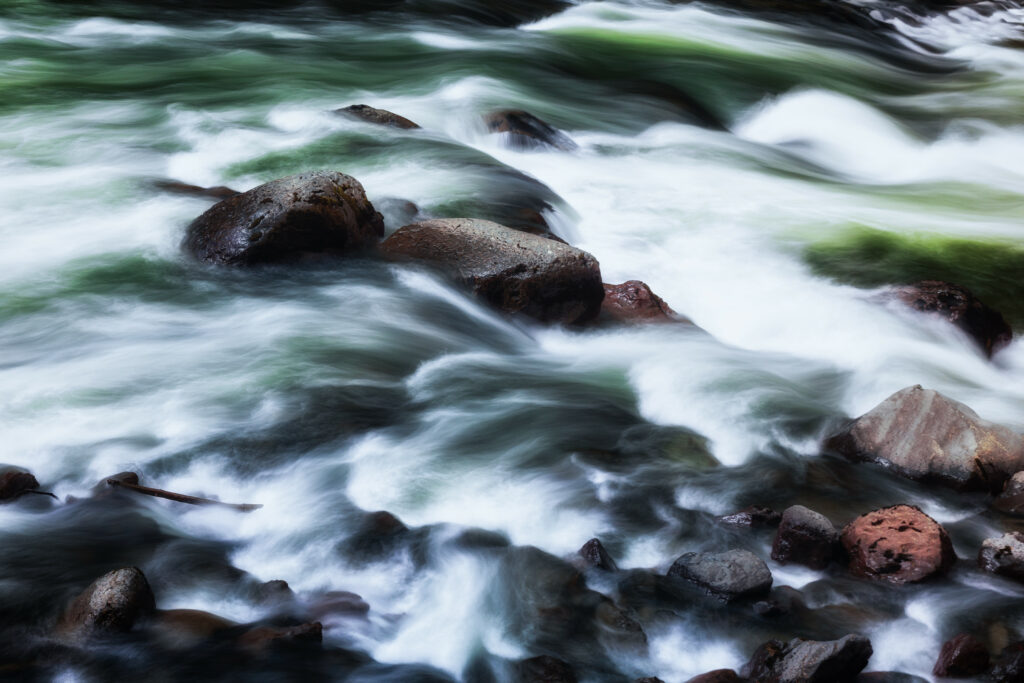High-resolution wallpaper of crystal-clear river flowing over smooth dark stones in nature