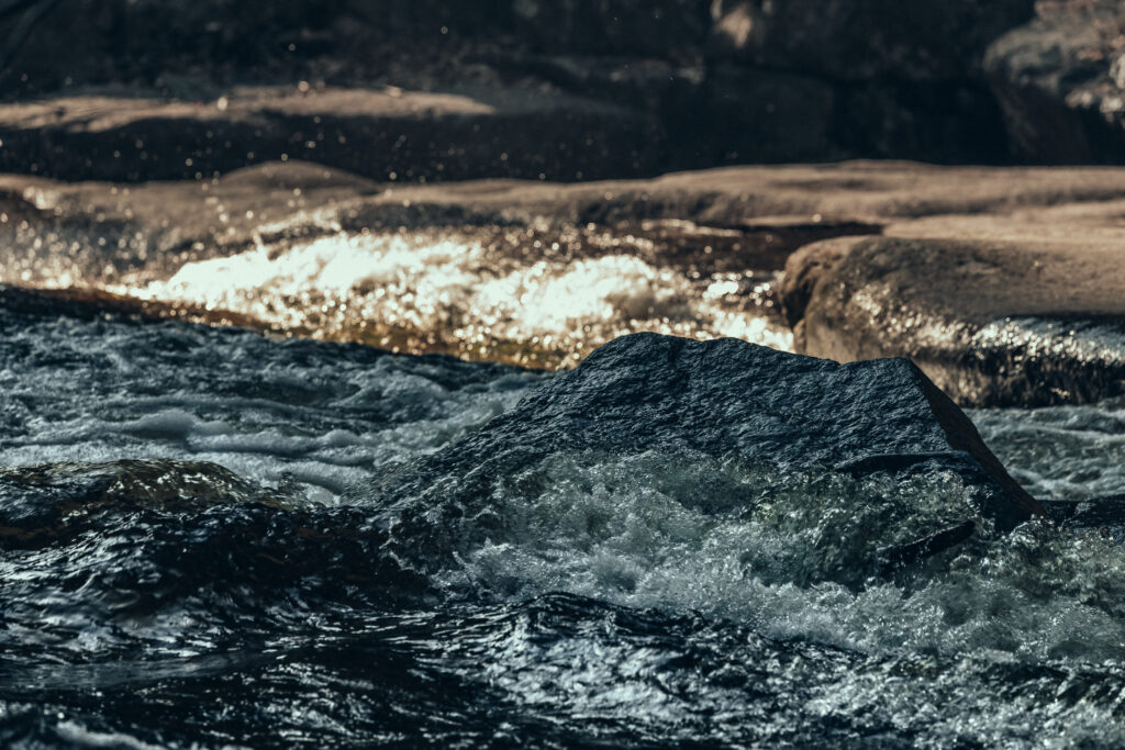 Serene river flowing over smooth stones with clear water sprays sunlight on natural textures wallpaper
