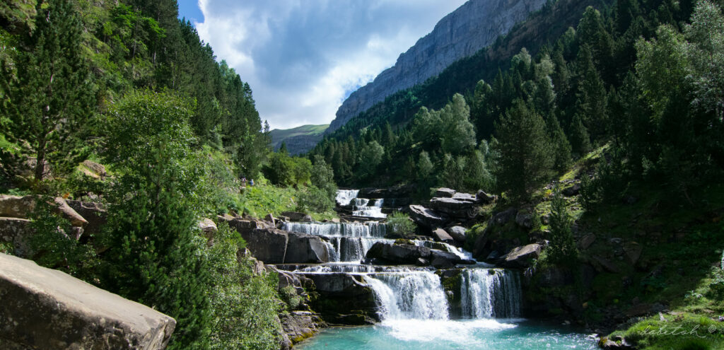Tranquil river flowing over smooth stones with lush green trees and mountain cliffs wallpaper