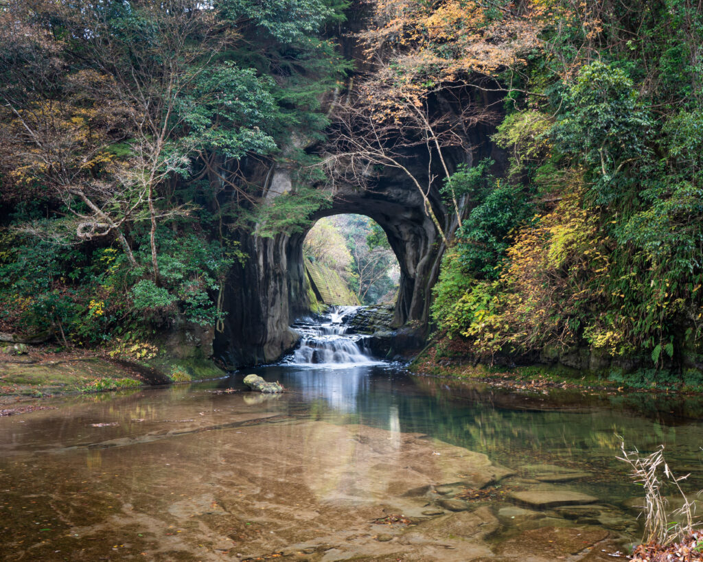 Tranquil river flowing through stone arch with lush trees vibrant greenery and waterfall reflection Wallpaper