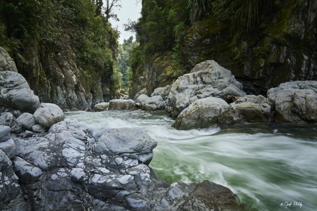 Serene river flowing over smooth grey rocks surrounded by lush greenery and steep cliffs wallpaper