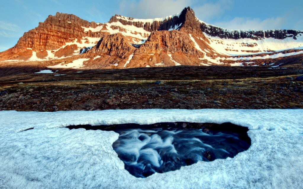 Vibrant river flowing through snowy crust with rugged mountains in soft natural light wallpaper