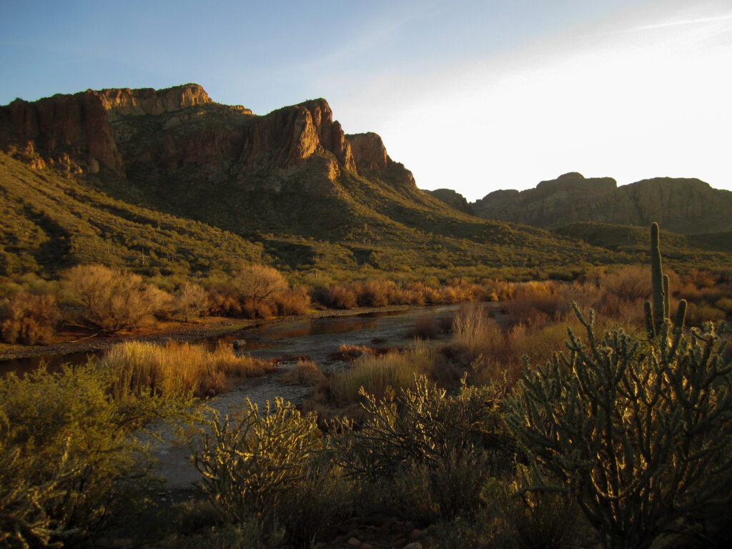 Serene river winding through rocky terrain with desert trees and mountains at sunset wallpaper