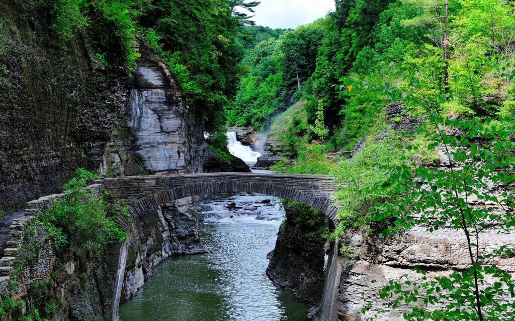 Serene river winding through rocky cliffs with stone bridge and lush green trees landscape wallpaper