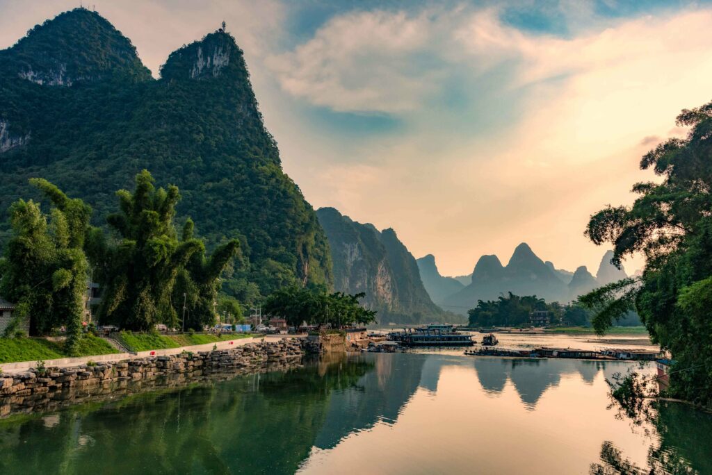 Serene river reflecting lush green trees and rocks under pastel sky natural landscape wallpaper