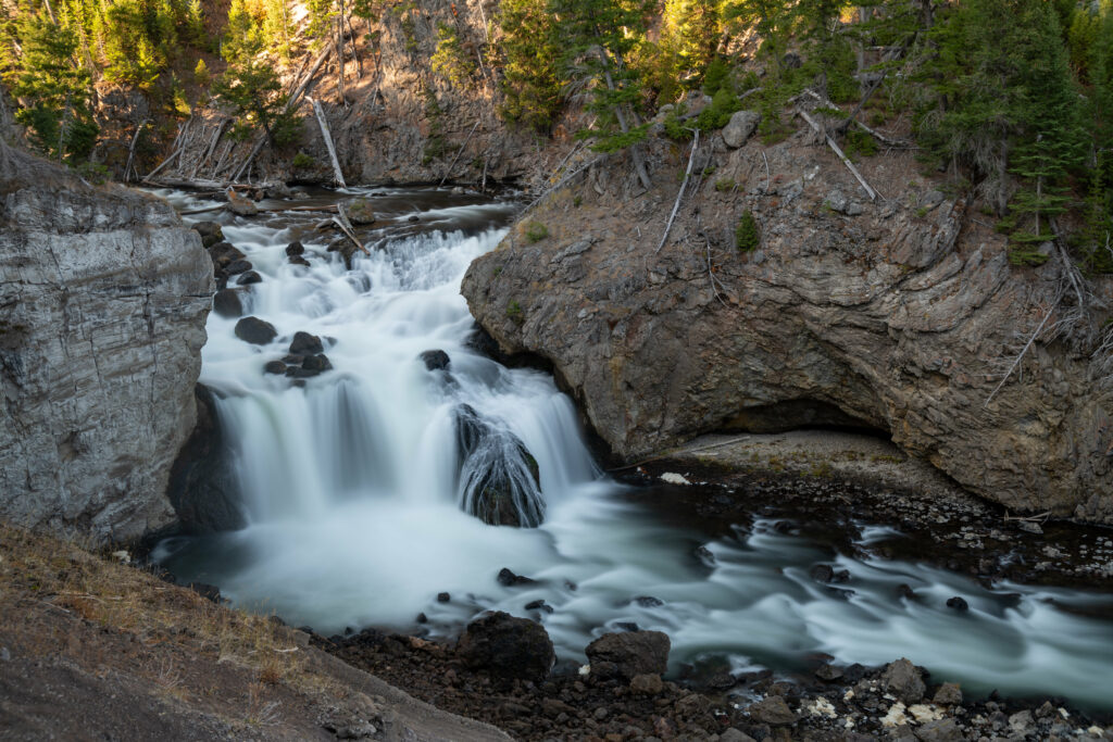 Silky smooth river flowing over rocks by cliffs and green trees in serene natural landscape wallpaper
