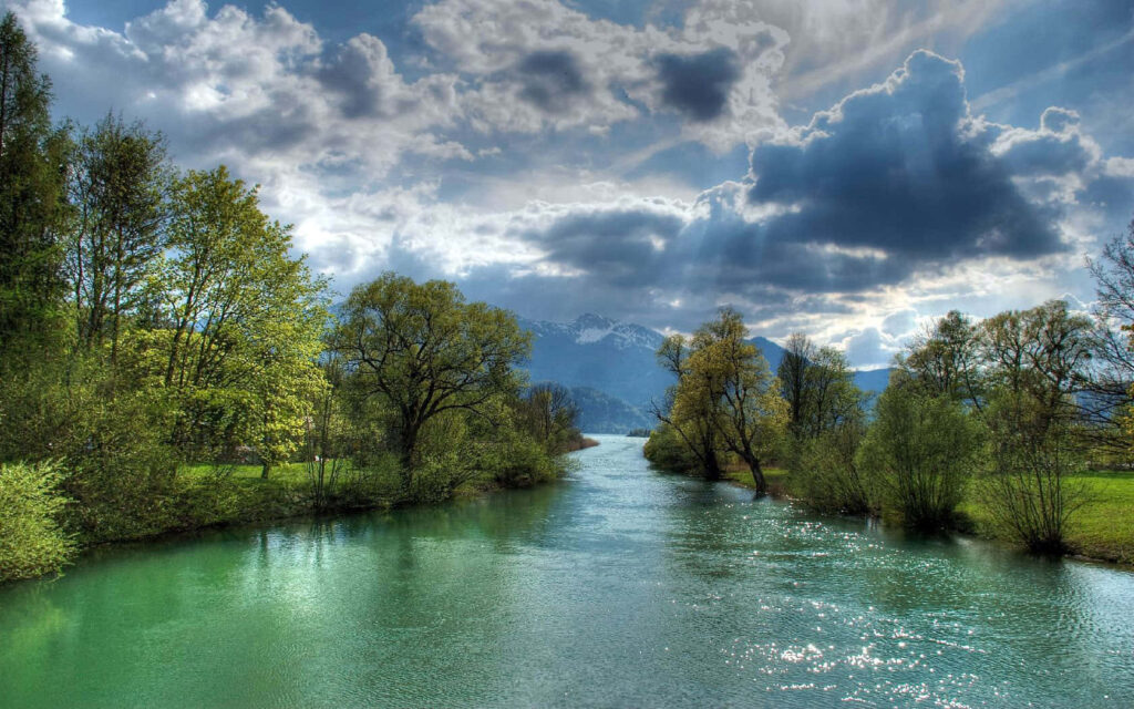 Serene River Wallpaper: Lush Greenery & Dramatic Cloudy Sky