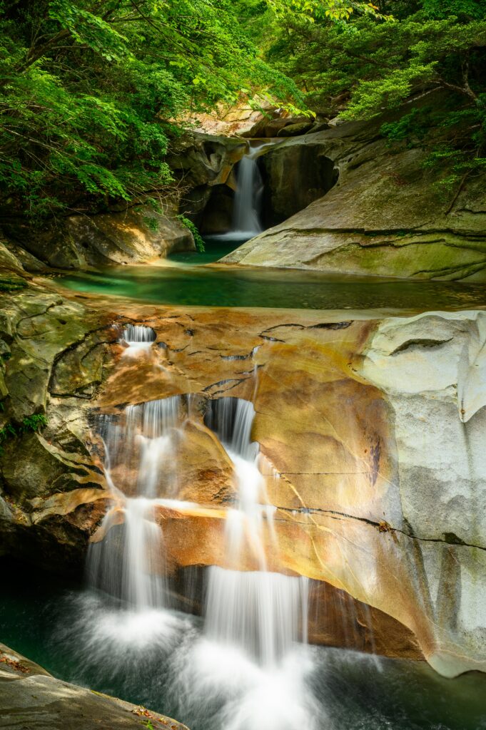 Tranquil river cascading over stone cliffs with waterfalls surrounded by lush green forest trees Wallpaper