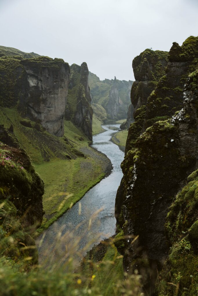 Serene river flowing through mossy rocks and tall cliffs surrounded by lush green nature landscape Wallpaper