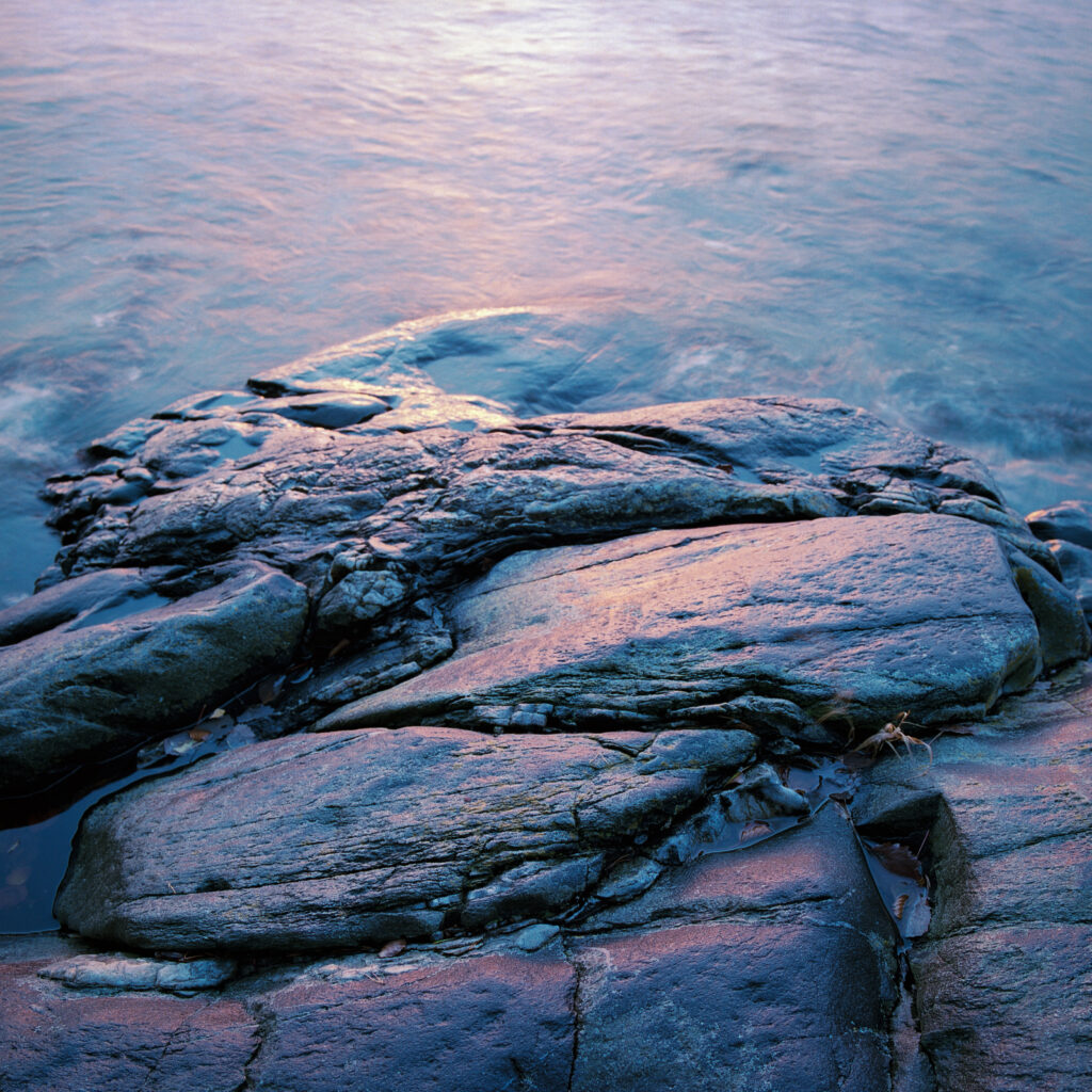 Rugged wet stones with deep textures under flowing water in soft blue and purple tones riverside Wallpaper