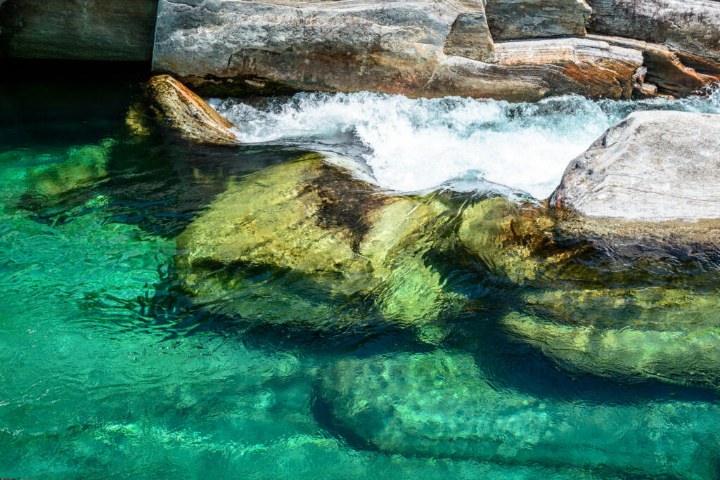 Tranquil riverside with smooth stones under clear turquoise water and sunlight reflections wallpaper