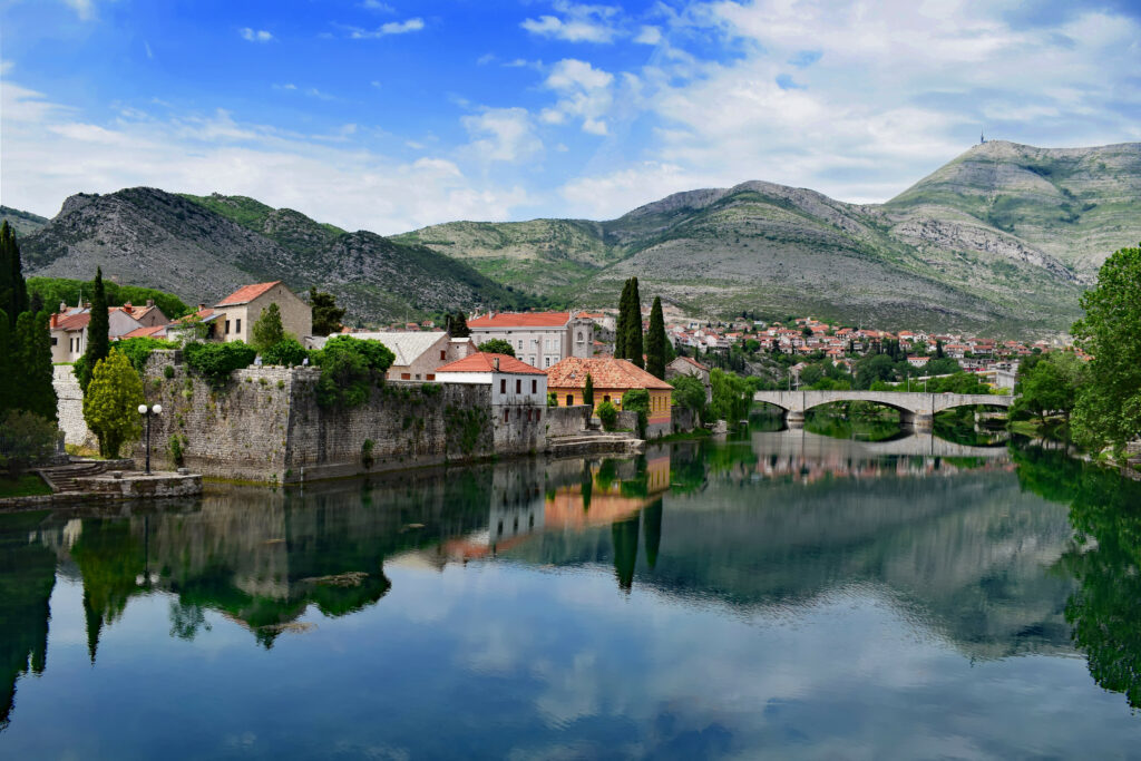 Serene riverside village with red roofs stone bridge lush green mountains vibrant blue sky wallpaper