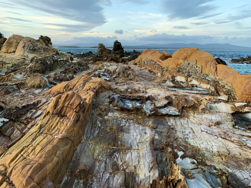 Rugged coastal rocks and calm blue sea under soft cloudy sky serene natural wallpaper background