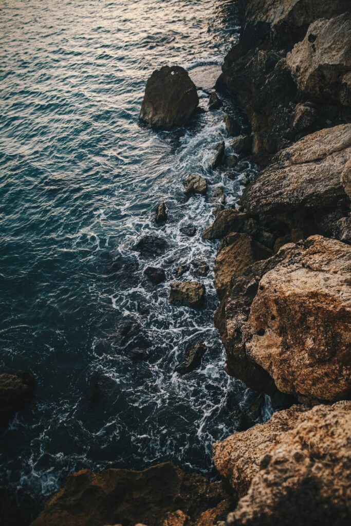 Rugged coastline with deep blue waves crashing on textured rocky cliffs under natural light Wallpaper