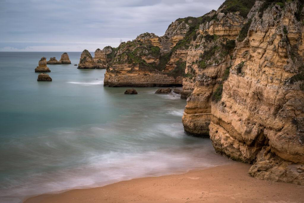 Serene coastline with rugged cliffs rock formations calm sea sandy beach and moody overcast sky wallpaper