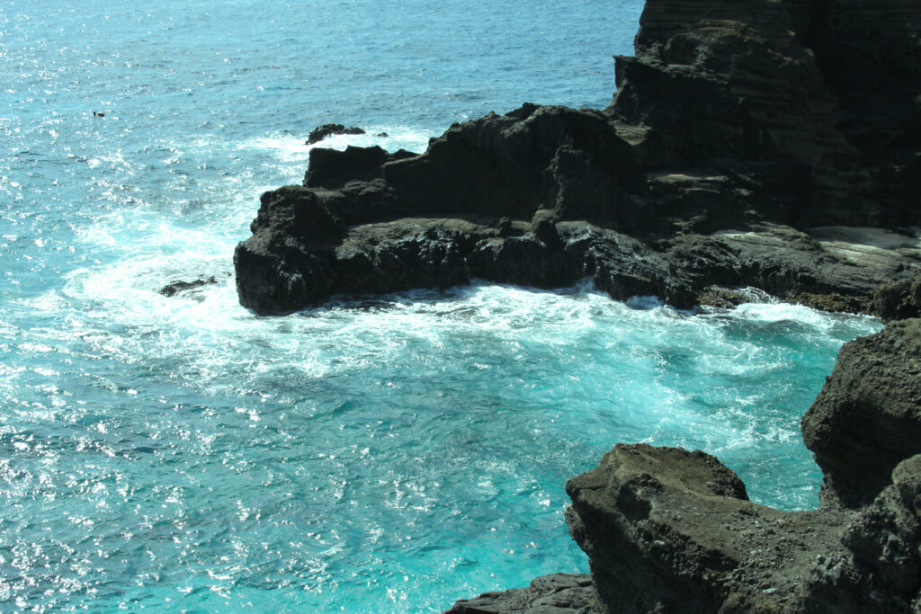 Rugged rocky coastline with turquoise waves glistening under sunlight serene nature wallpaper