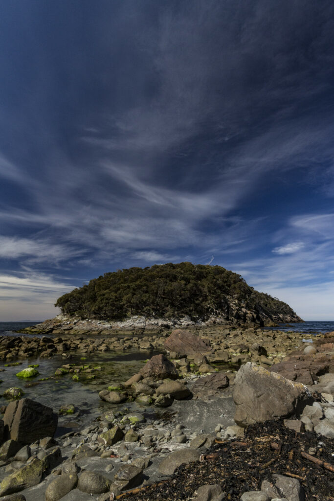Rugged island with rocky shore and lush greenery under dramatic cloudy sky coastal wallpaper