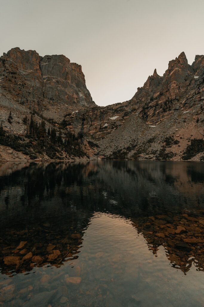 Serene dusk landscape with rugged mountains and calm lake reflecting rocky cliffs and shoreline Wallpaper