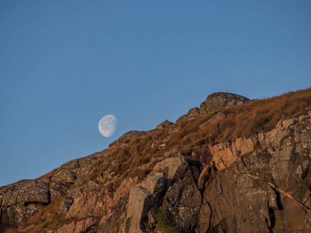 Moonlit rugged rock formations and earthy textured stones under a clear blue sky wallpaper background