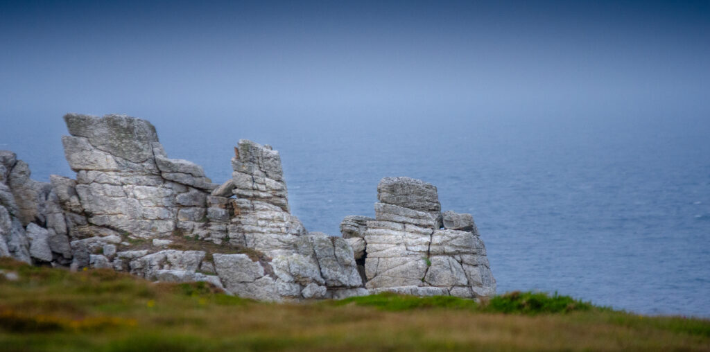 Rugged stone formations and grassy ruins by calm blue sea under soft natural light wallpaper background