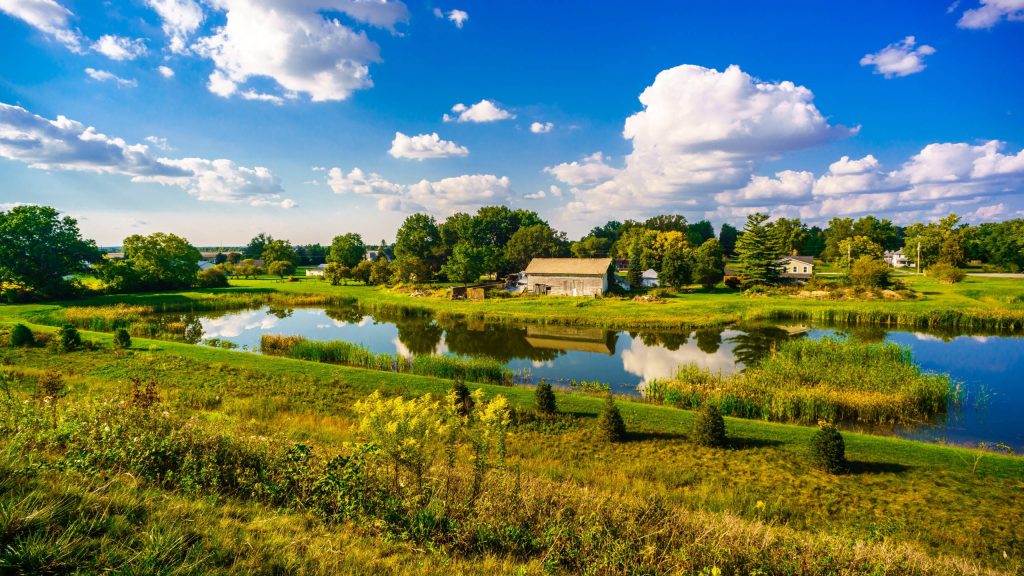 Rustic wooden barn by reflective pond with green meadows and blue sky rural farm wallpaper