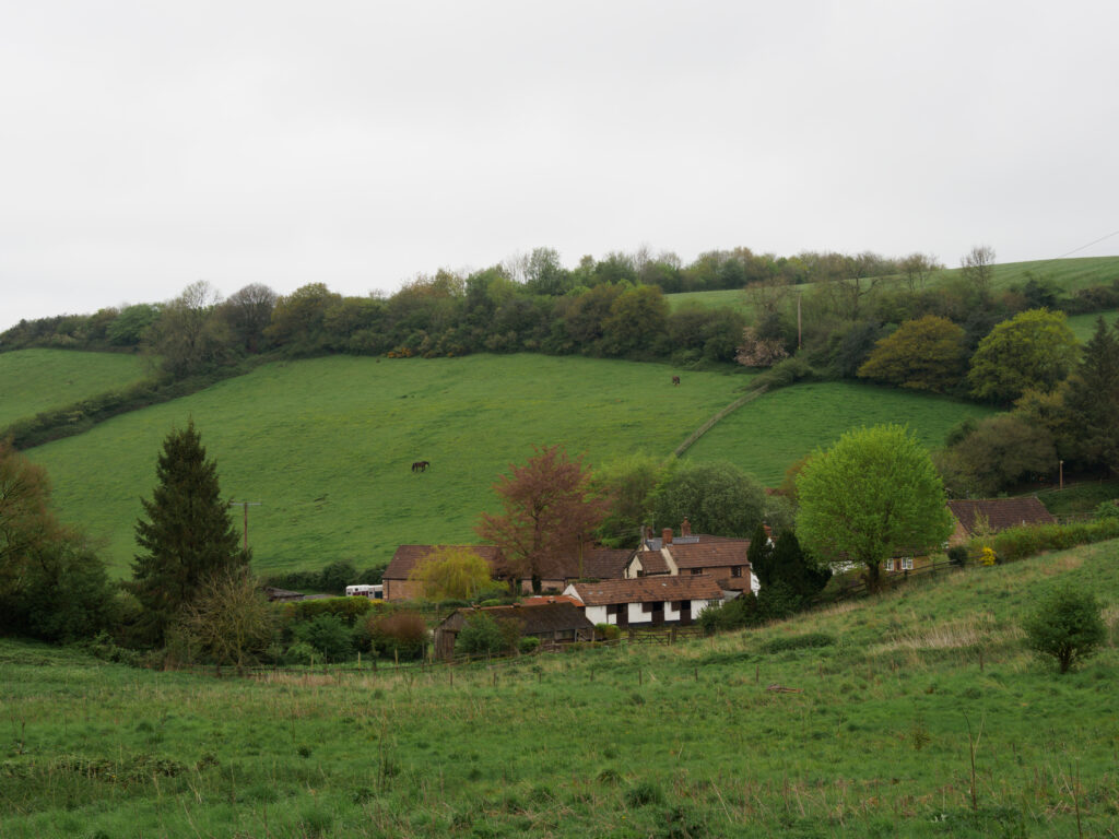 Quaint houses by lush rolling hills with vibrant grass and scattered trees under cloudy sky wallpaper