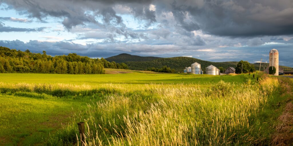 Serene rural landscape with green fields rolling hills farm silos rustic buildings dramatic sky Wallpaper