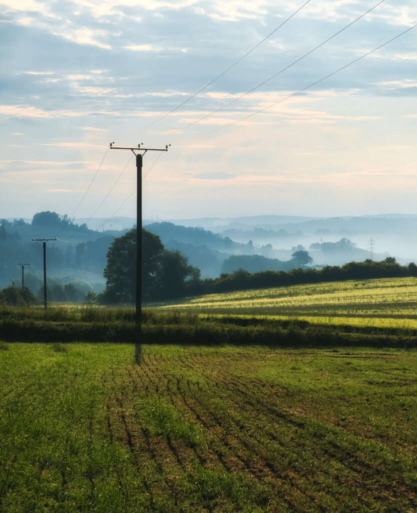 Serene green field with tall utility poles and wires under cloudy sky rural landscape wallpaper