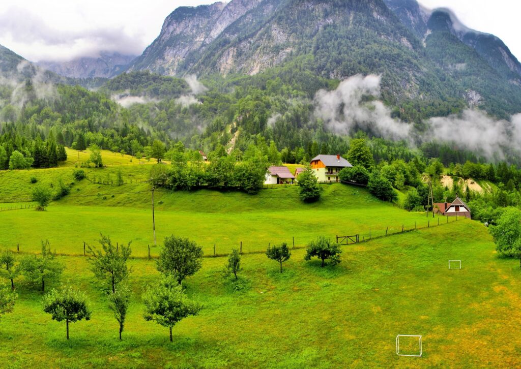 Serene rural Slovenia landscape with green fields trees forests misty mountains and quaint houses Wallpaper