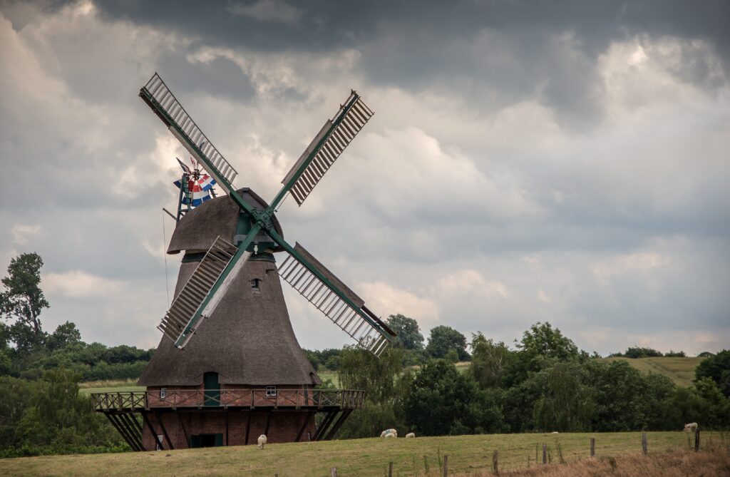Traditional windmill with green fields and grazing sheep under a dramatic cloudy sky wallpaper