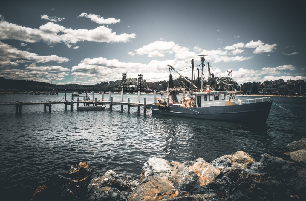 Rustic boat docked by wooden pier on calm sea under cloudy sky serene coastal wallpaper background