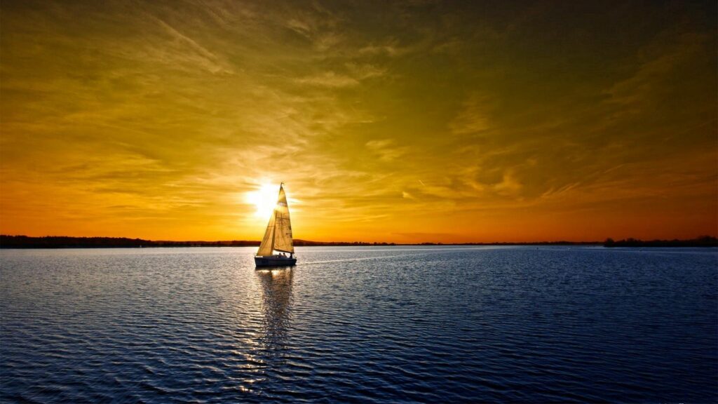 Serene sailboat on calm sea at golden sunset with warm sky reflections peaceful wallpaper background