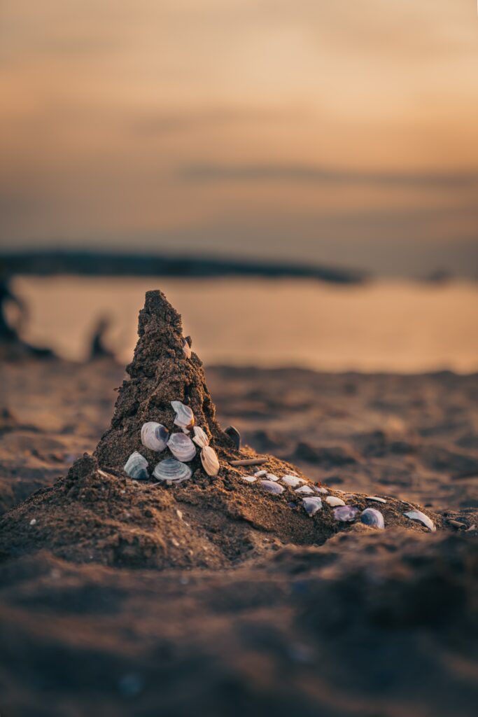 Close-up of small sandcastle with conch shells on beach at calm sea sunset wallpaper background