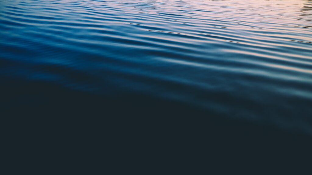 Serene sea surface wallpaper with gentle ripples soft blue hues and subtle sunset colors background