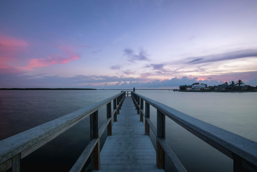 Serene Shoreline: A Gray Wooden Bridge Amidst a Calm Ocean and Blue Skies Wallpaper in UHD 4K 4904x3269 Resolution