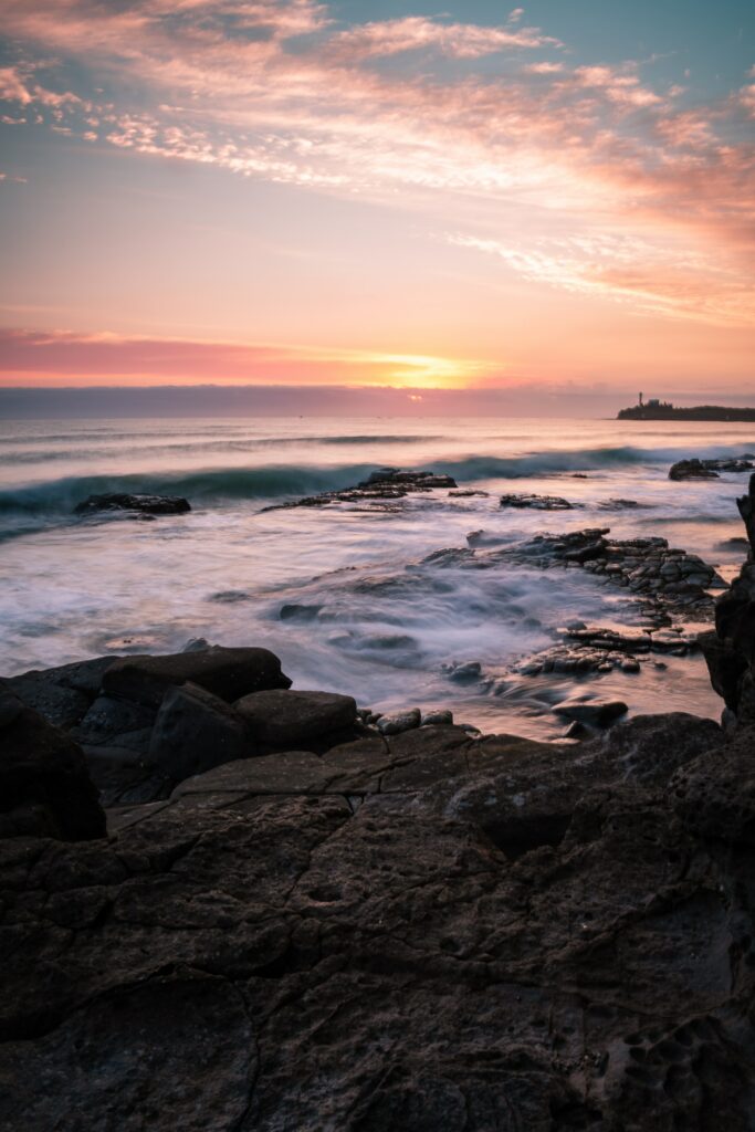 Serene seascape wallpaper with rugged rocks gentle waves warm sunset and colorful sky
